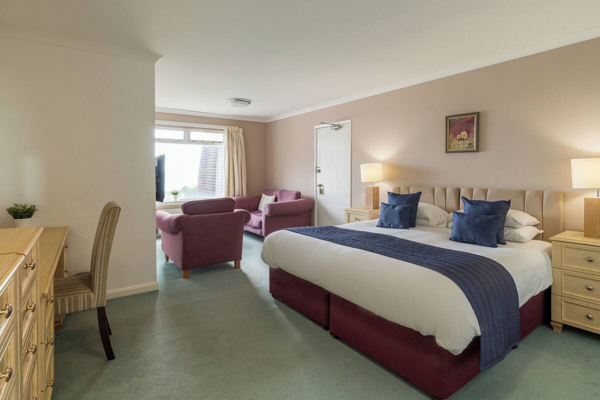 A hotel room with a large bed, two bedside tables, a desk, a chair, and a window with curtains.