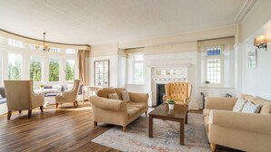 A spacious living room with a fireplace, large windows, and a high ceiling. - Northfield Hotel (Minehead)