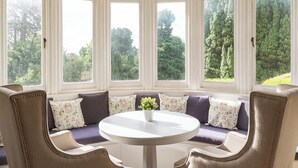 A bay window seating area with a round table, cushioned chairs, and a potted plant. - Northfield Hotel (Minehead)