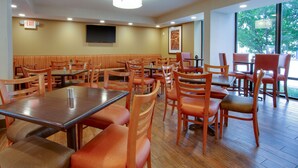 A restaurant with wooden tables and chairs, a flat-screen TV on the wall, and large windows with a view of trees. - Drury Inn & Suites Terre Haute (Terre Haute)