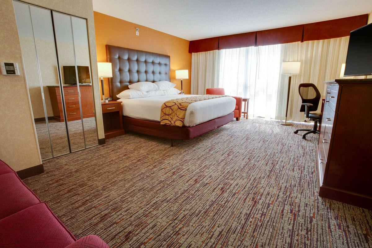 A hotel room with a large bed, a desk, a chair, a TV, a wardrobe, and a mirror.