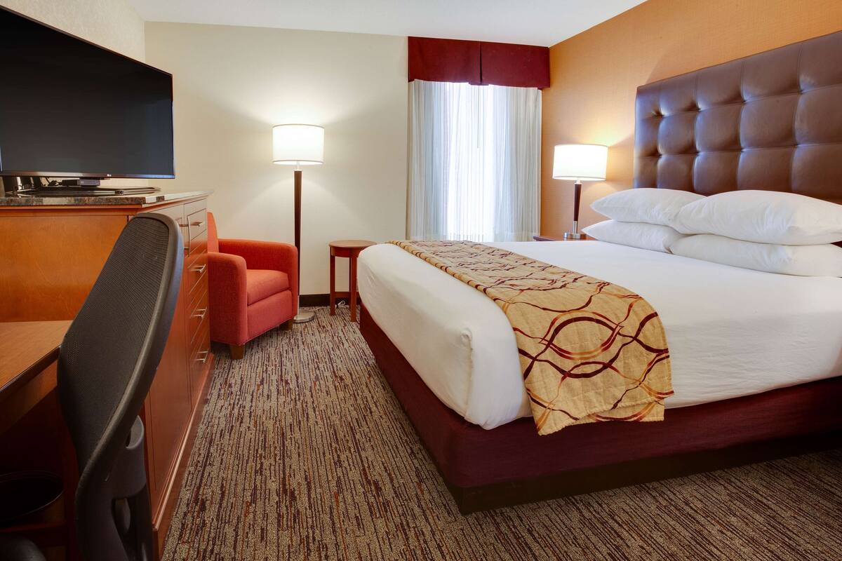 A hotel room with a large bed, a desk with a chair, a television, and two lamps.
