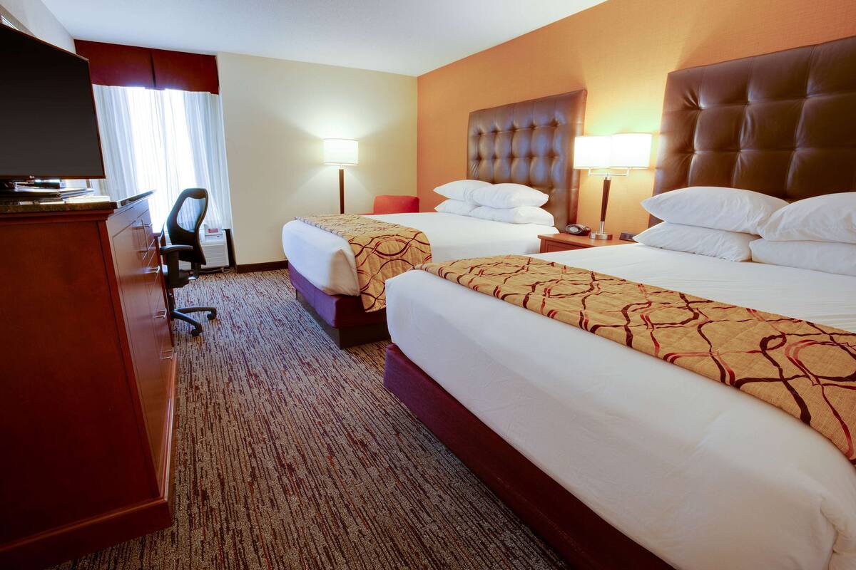 A hotel room with two beds, a TV, a desk, and a chair.