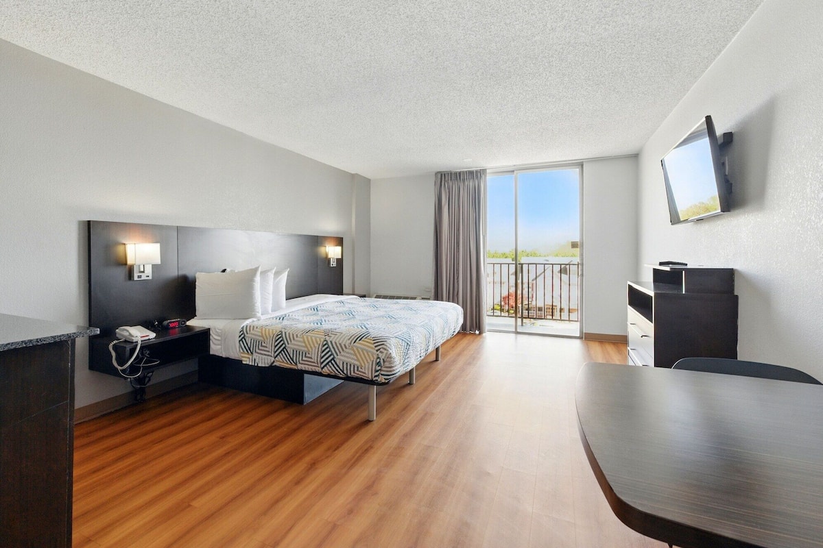 A hotel room with a bed, bedside table, lamp, TV, and a balcony with a view.