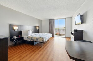 A hotel room with a bed, bedside table, lamp, TV, and a balcony with a view. - Motel 6 Atlanta, GA - Atlanta Airport (Atlanta)
