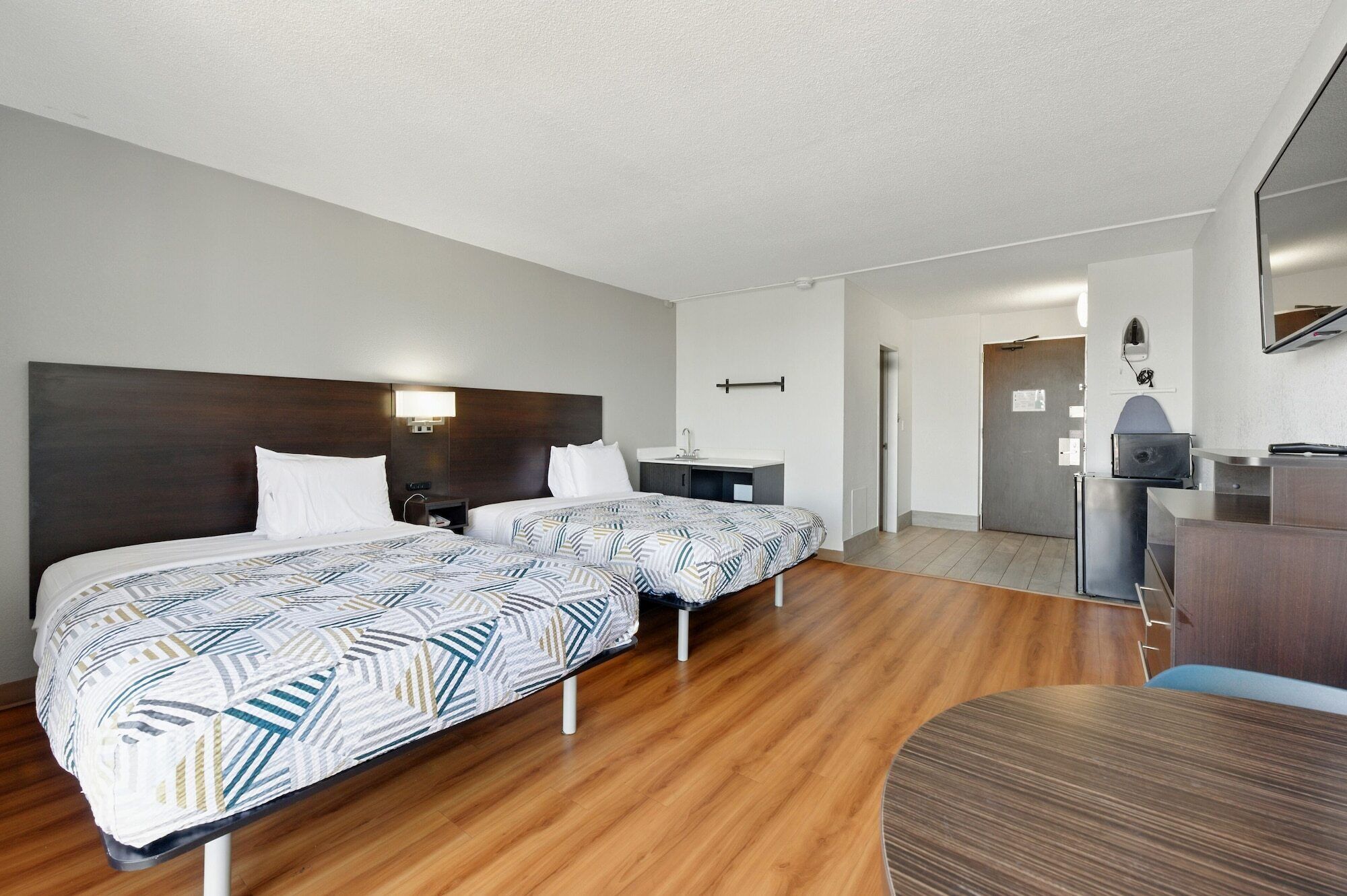 Habitación de hotel con dos camas, un escritorio, una silla, un televisor y un baño a la vista.