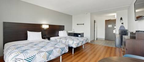 Habitación de hotel con dos camas, un escritorio, una silla, un televisor y un baño a la vista.