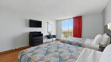 A hotel room with two beds, a desk with a chair, a TV mounted on the wall, and a balcony with a red curtain.