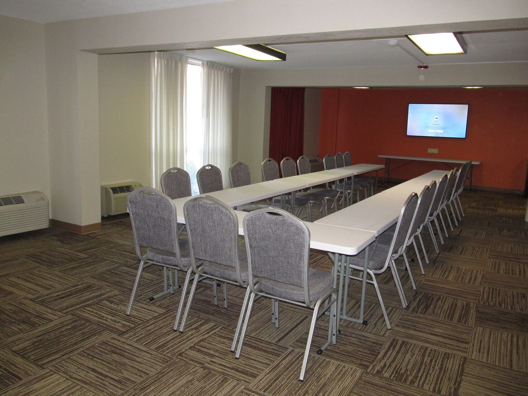 A conference room with a long table, chairs, a projector screen, and a carpeted floor.