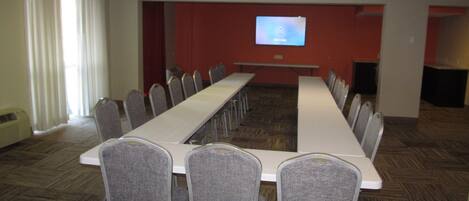 A conference room with a long table, chairs, a projector screen, and a whiteboard.