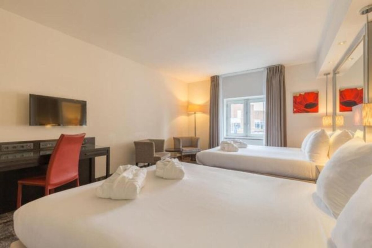 Habitación de hotel con dos camas, un escritorio con una silla, un televisor y una ventana con cortinas.