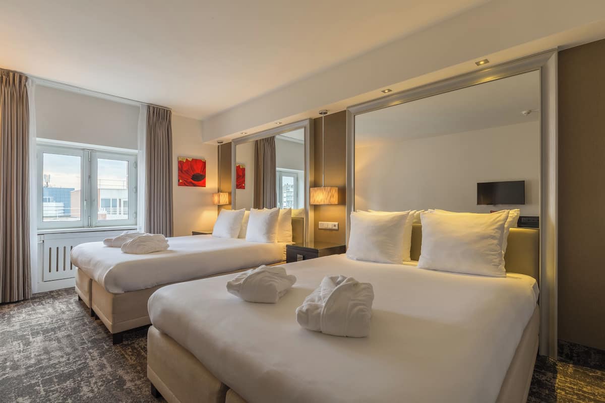 A hotel room with two beds, a large mirror, and a window with curtains.