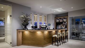 A modern reception area with a wooden counter, bar stools, and a potted plant.