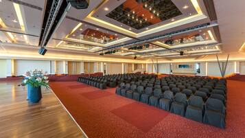 Een ruime zaal met rijen stoelen, een podium met lichtinstallatie en een rode loper.