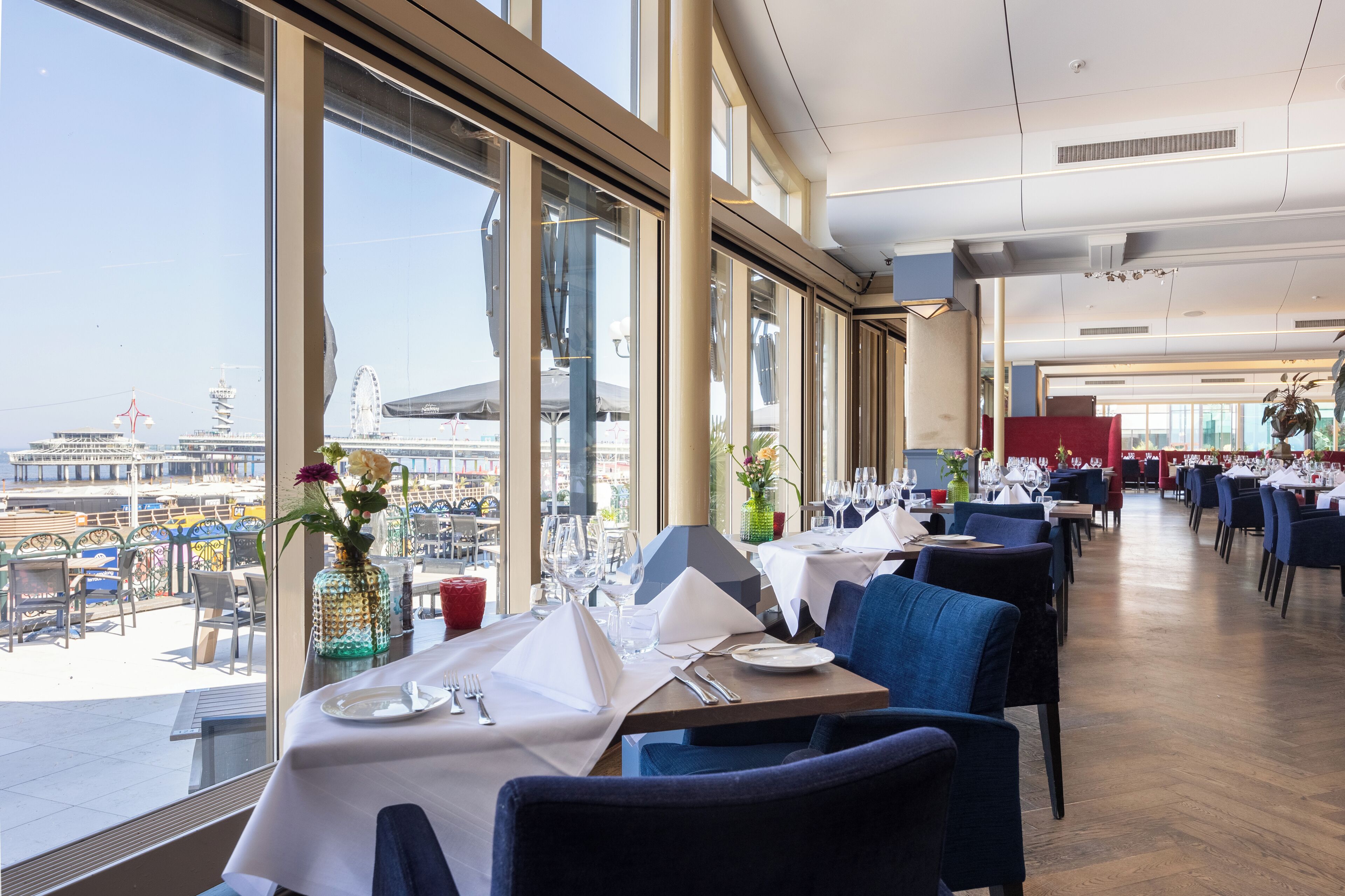 A restaurant with tables set for dining, large windows offering a view of the cityscape, and a modern interior design.