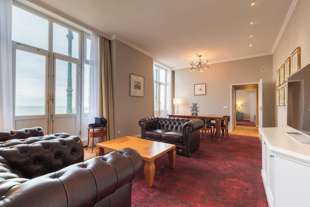 A spacious living room with a red carpet, leather sofas, a wooden coffee table, and a chandelier.