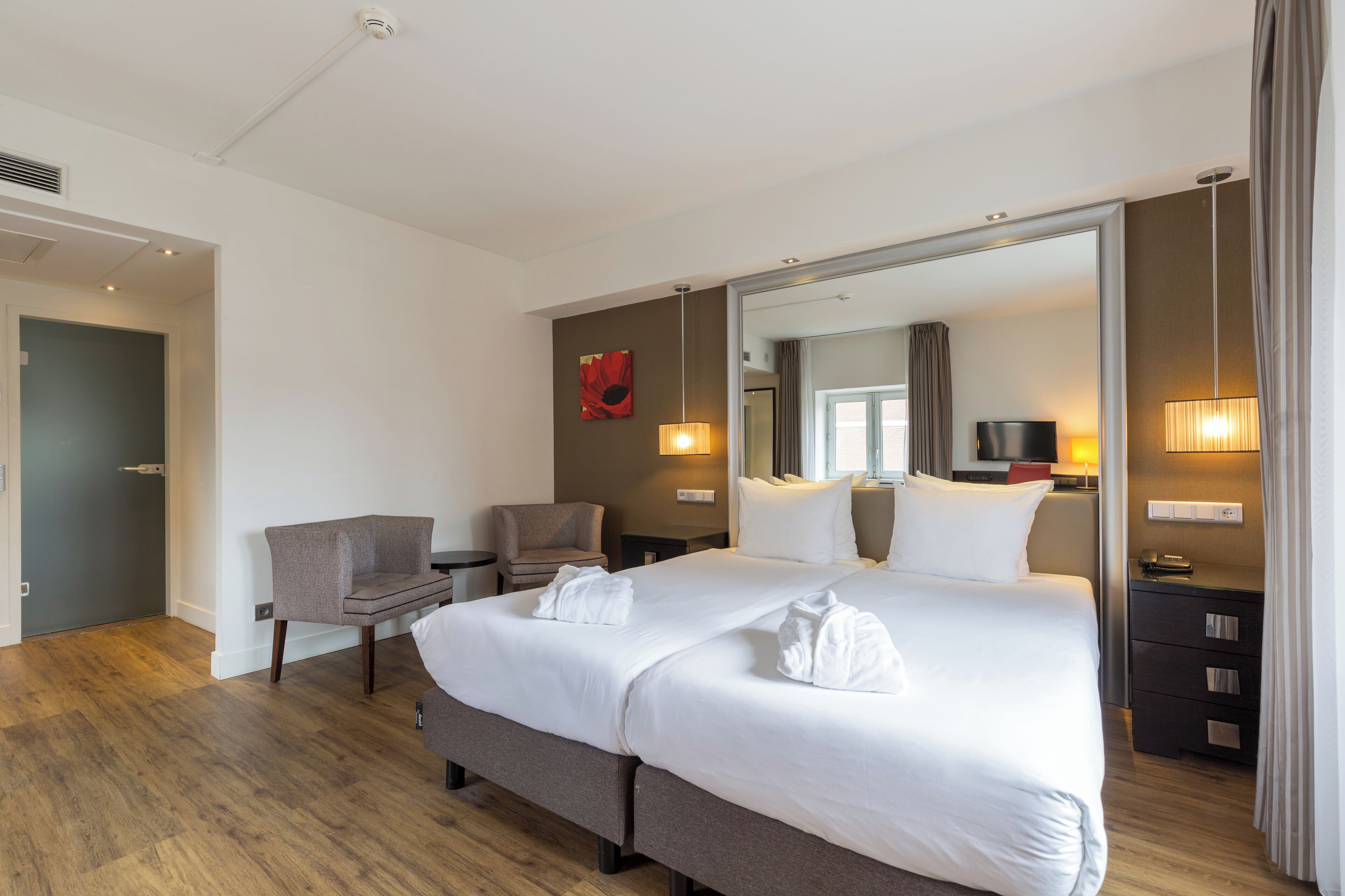 A hotel room with a large bed, a chair, a desk, and a mirror.