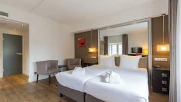 A hotel room with a large bed, a chair, a desk, and a mirror.