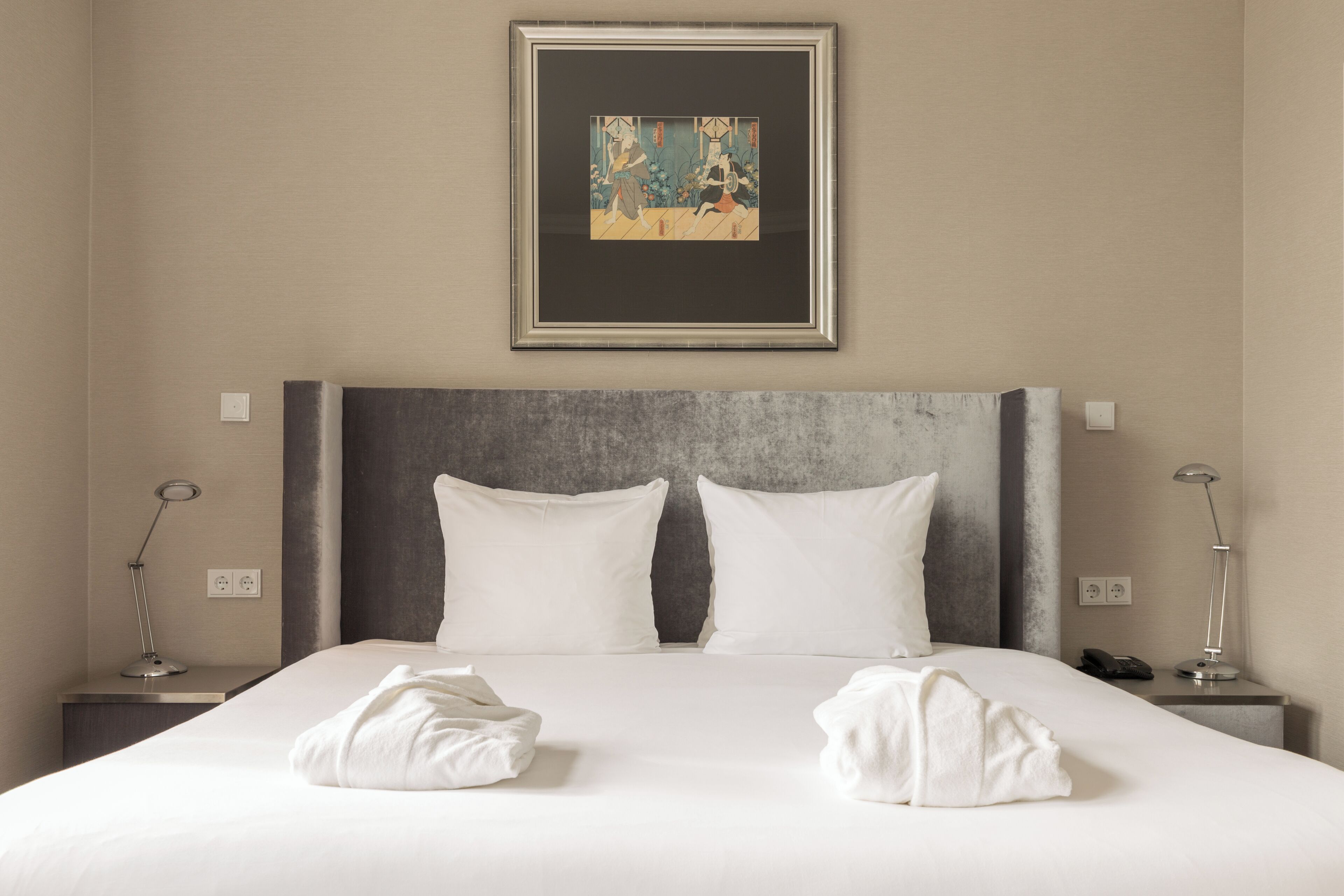 Un lit bien fait, avec du linge de lit blanc, une œuvre d’art encadrée au-dessus et des lampes de chevet de chaque côté.