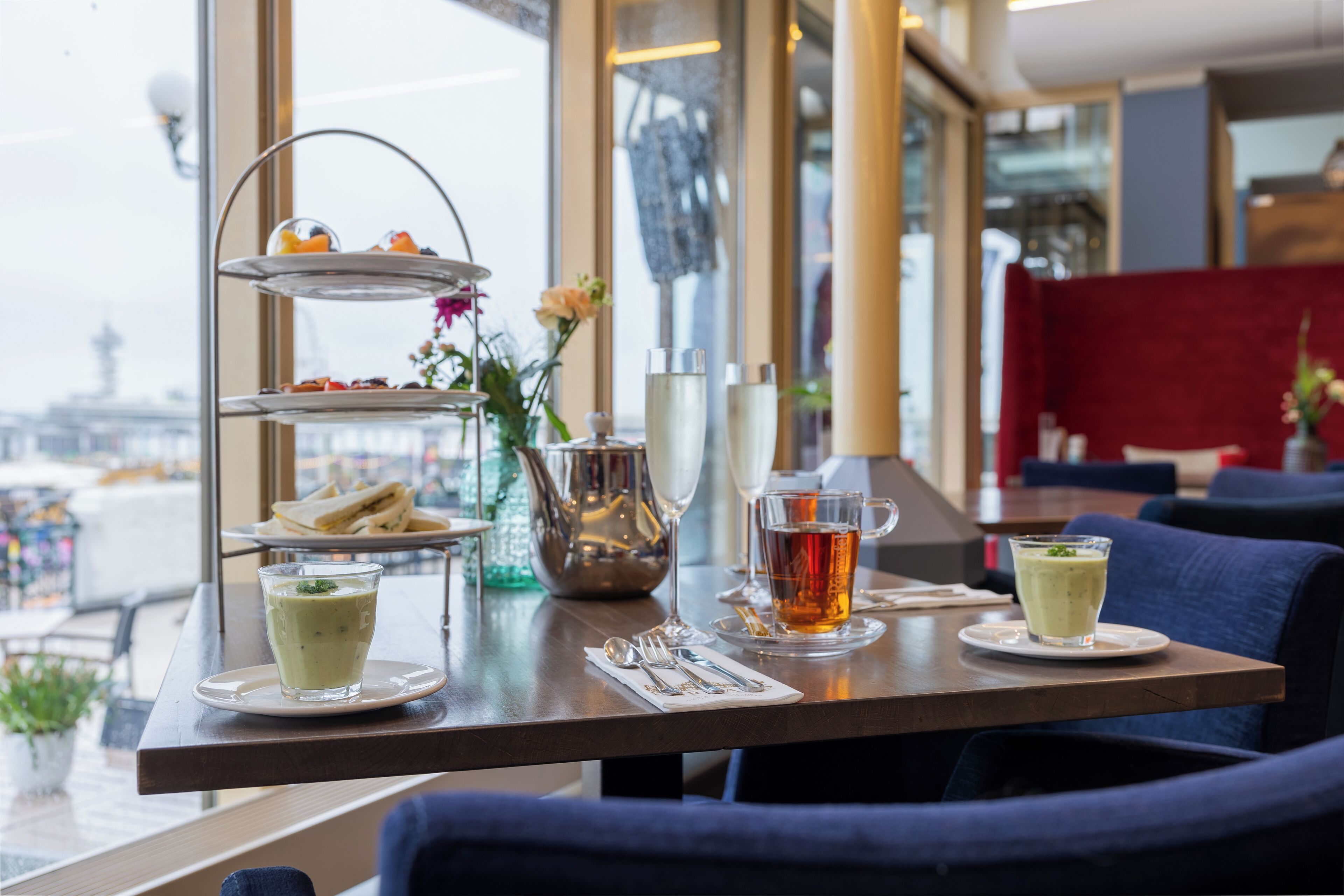 Une table à manger avec un présentoir à étages rempli de pâtisseries, une carafe et deux verres de thé.