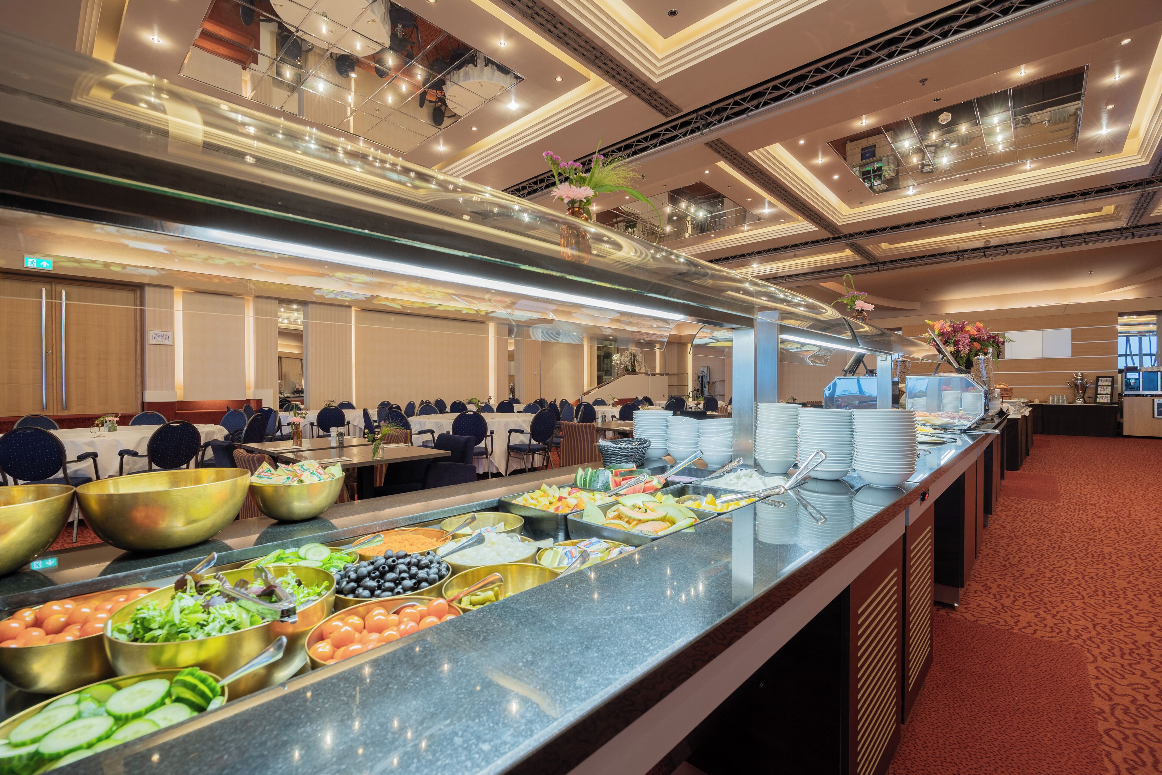 Zona de buffet con varias estaciones de comida, que incluyen ensaladas, frutas y otros platos.