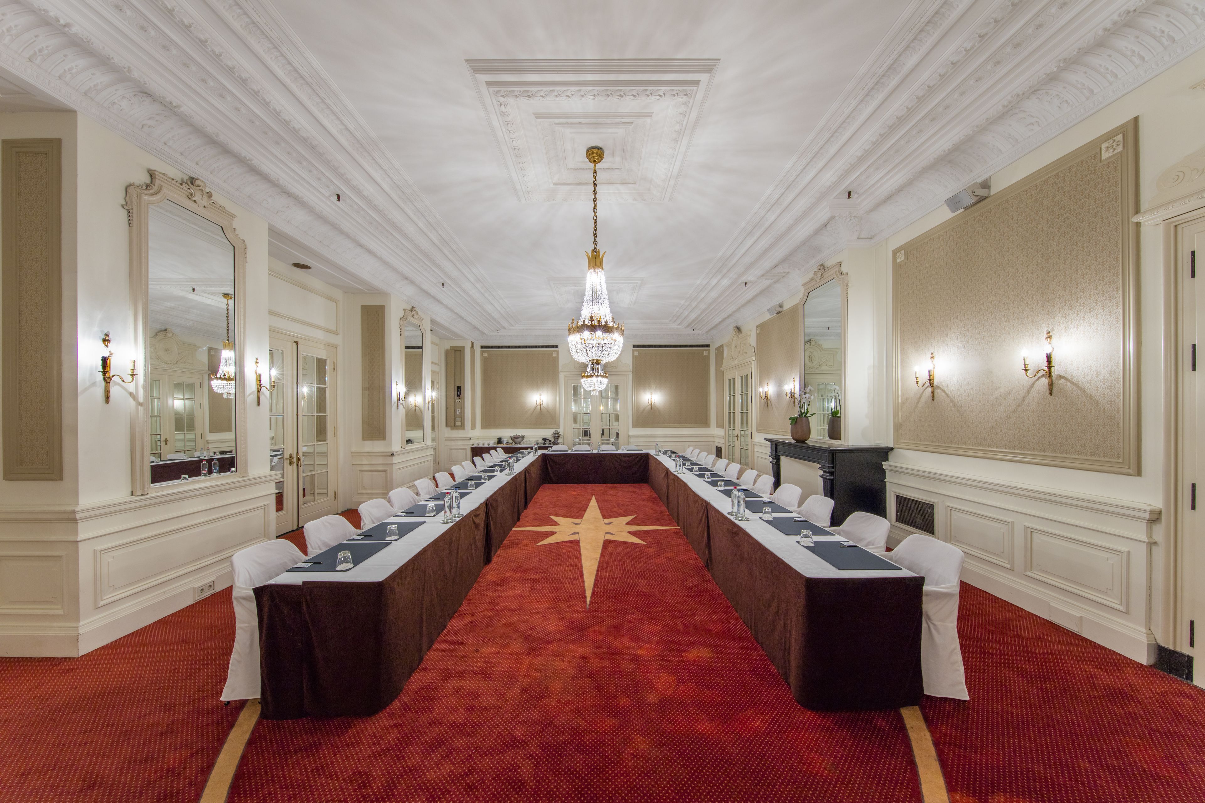 A conference room with a long table, white chairs, and a red carpet.