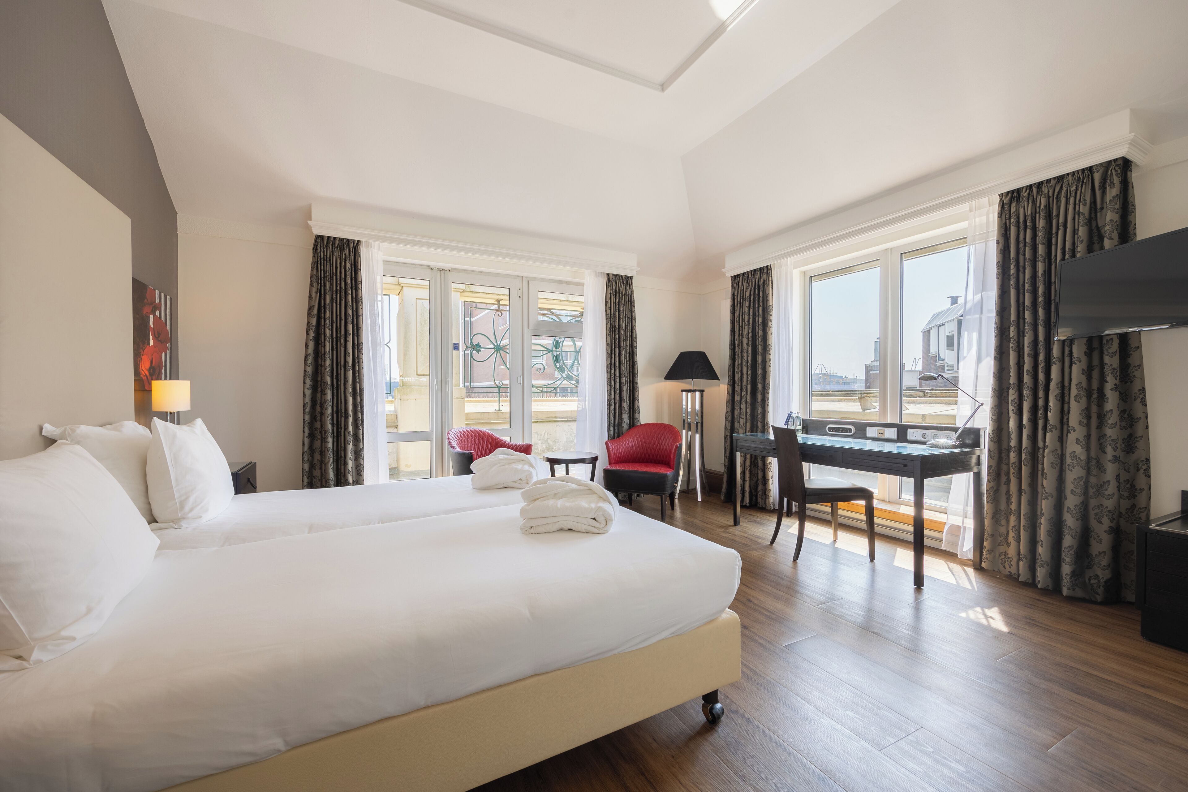 Quarto de hotel com uma cama grande, uma escrivaninha, uma cadeira e uma televisão.
