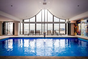Relax by the pool with a view of the city skyline, surrounded by lounge chairs and a vibrant mural.
