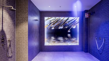 Experience a sleek, contemporary bathroom with a minimalist design, featuring a large mirror, modern shower system, and light-colored tiles.
