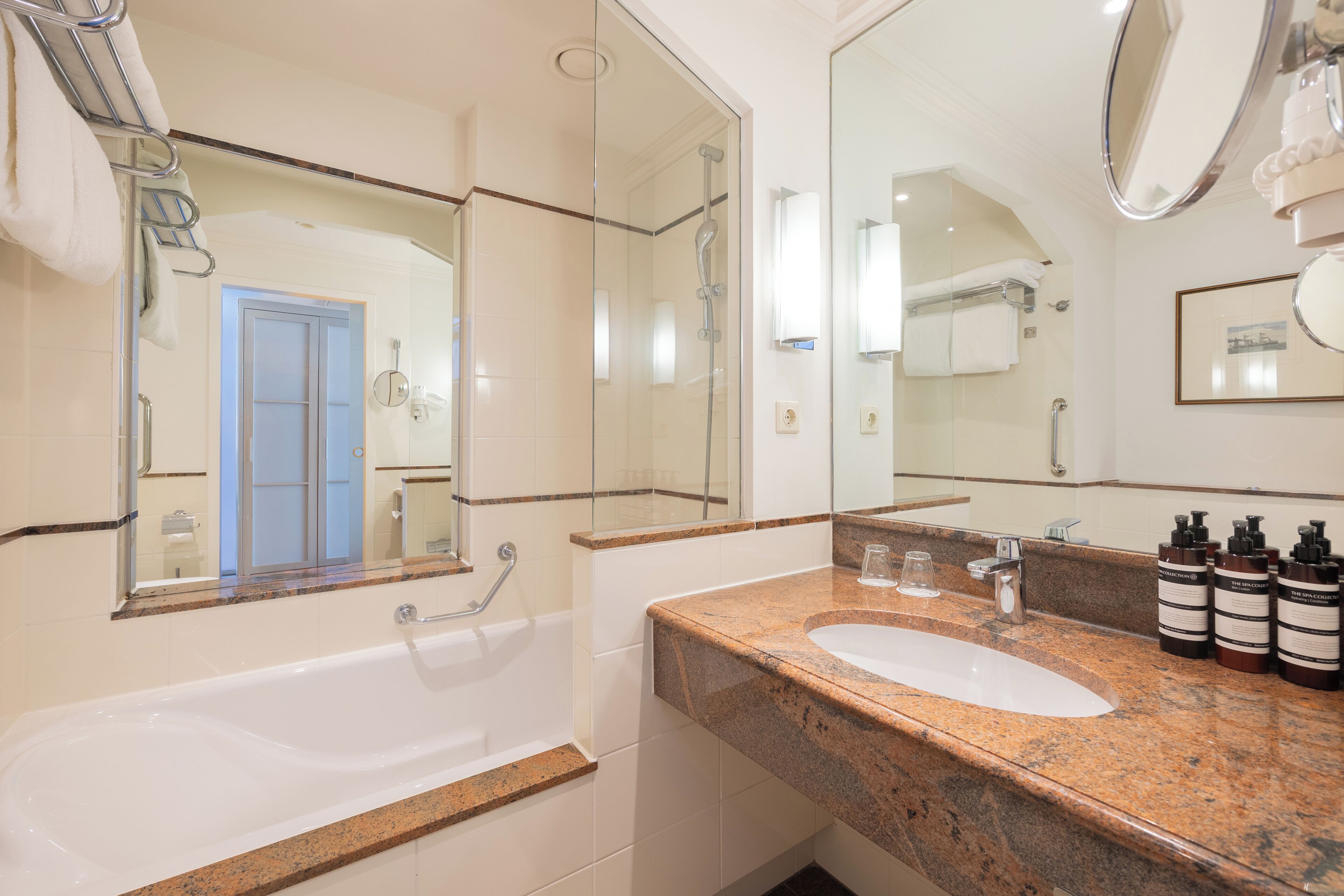 A bathroom with a white bathtub, a granite countertop, a sink, and a large mirror.