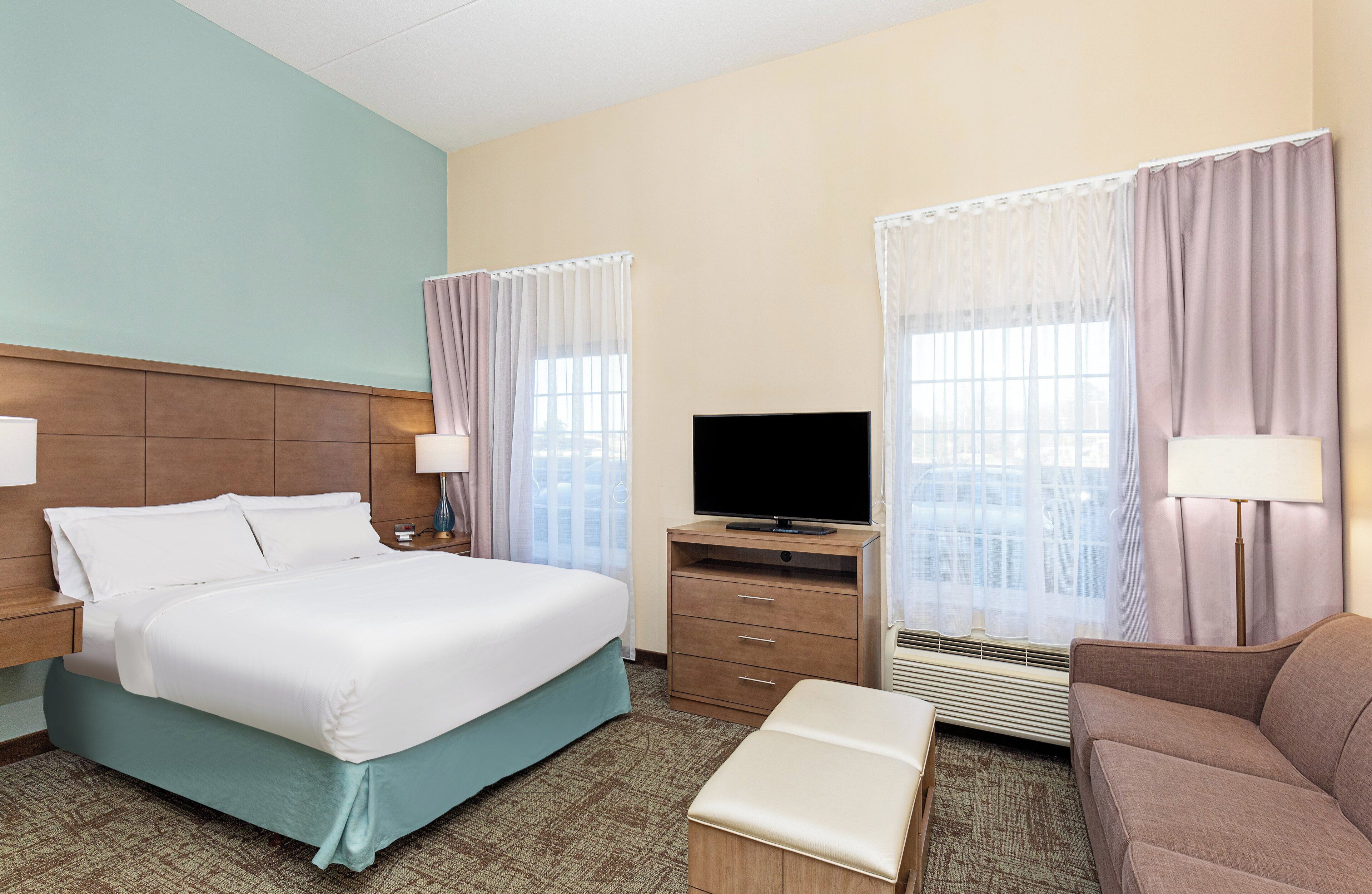 Quarto de hotel com cama, televisão, escrivaninha e cadeira.