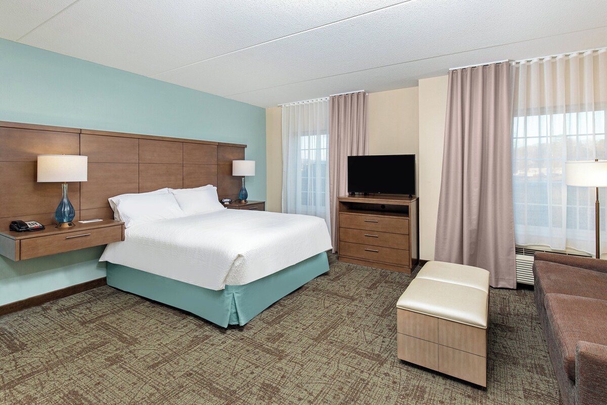 Una habitación de hotel con cama, mesitas de noche, televisor, sofá y una pequeña mesa.