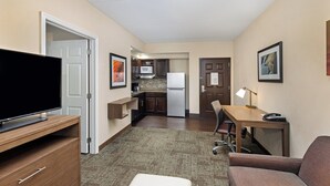 Habitación de hotel pequeña con televisión, kitchenette y escritorio con lámpara.