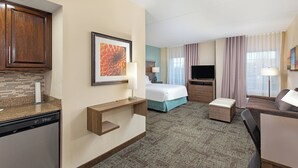 Habitación de hotel con kitchenette, cama, televisor y zona de estar.