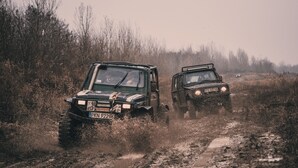 Dos vehículos todoterreno circulando por un sendero embarrado, rodeado de hierba alta y árboles.