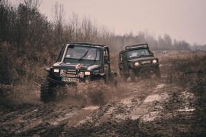 Dos vehículos todoterreno circulando por un sendero embarrado, rodeado de hierba alta y árboles.