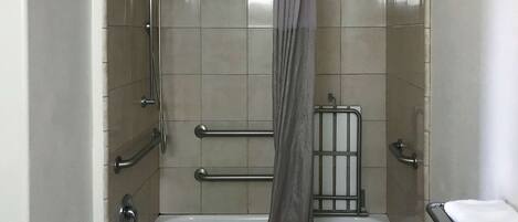 A bathroom with a bathtub, grab bars, a showerhead, and a towel rack.