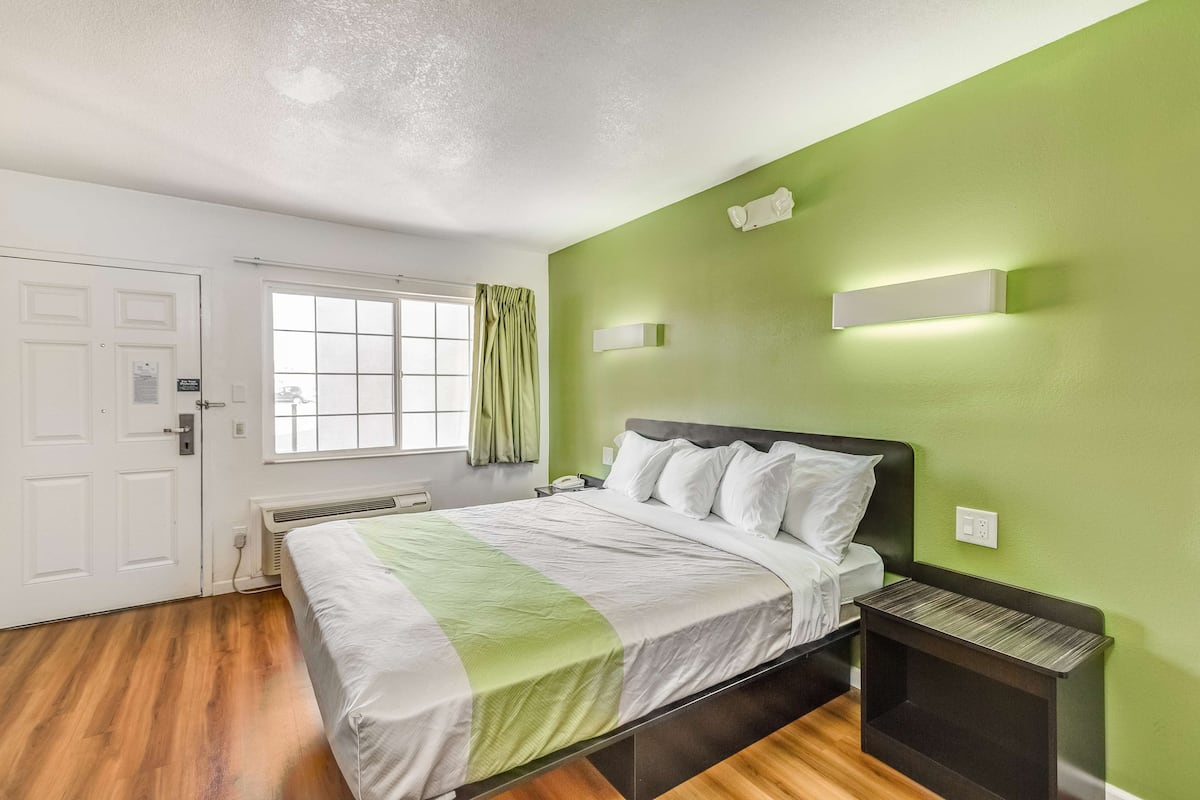 Un dormitorio con cama, mesita de noche, ventana con cortinas y pared verde.