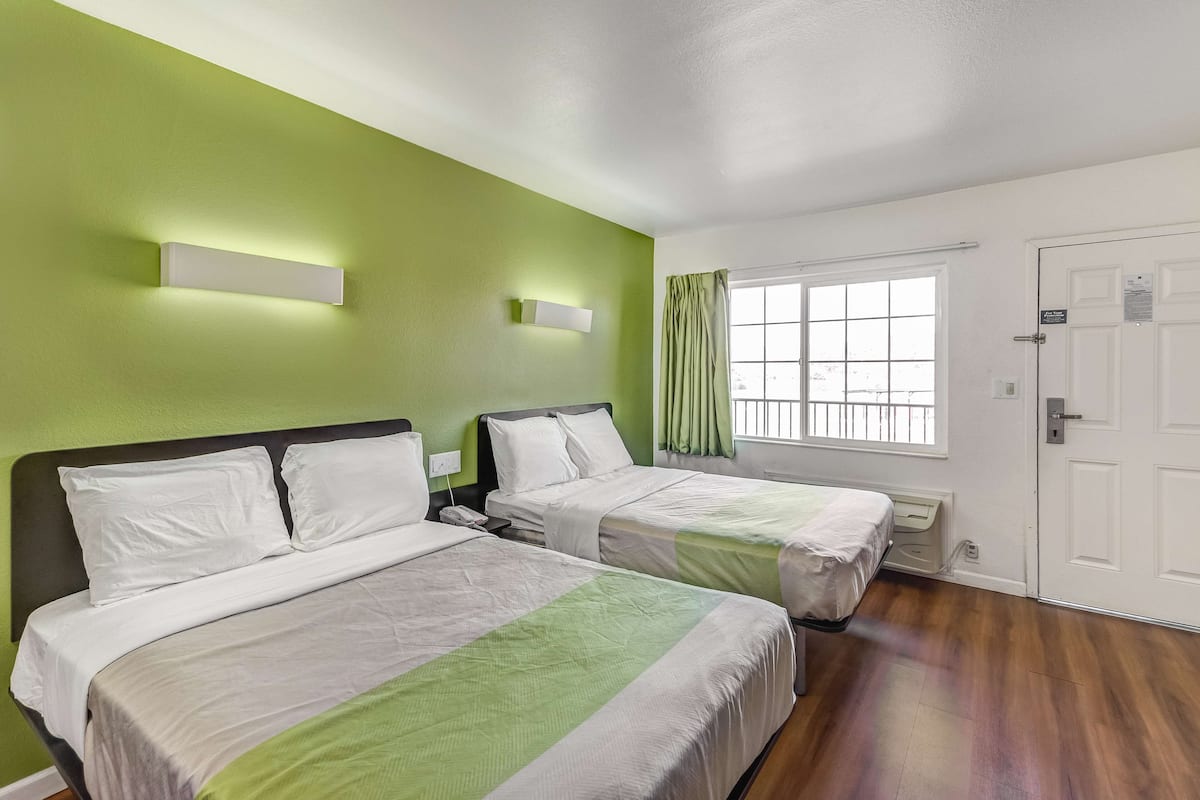 Habitación de hotel con dos camas, paredes verdes, una ventana con cortinas y una puerta blanca.