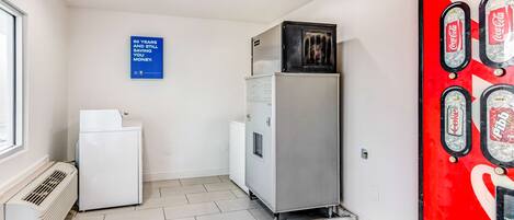 Una habitación con aire acondicionado blanco, un refrigerador plateado y una máquina expendedora de Coca-Cola.