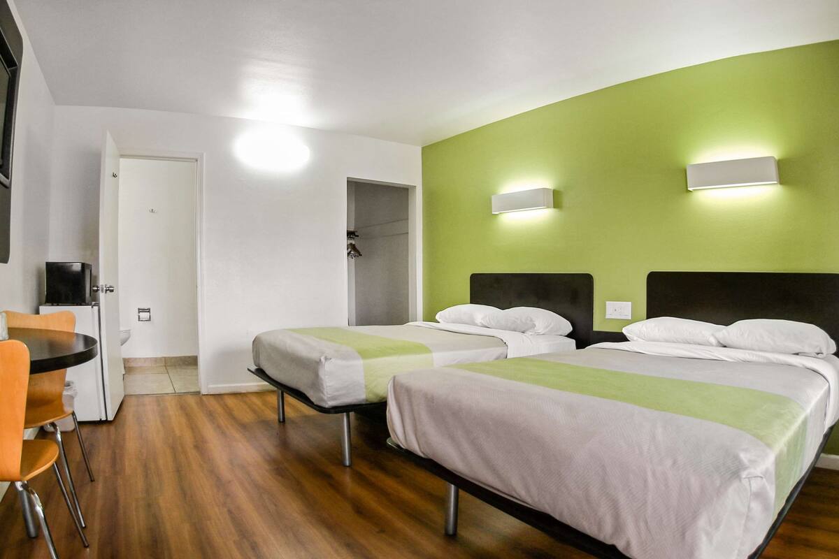 Habitación de hotel con dos camas, una mesita y una silla. Se ve una puerta que da al baño y un armario.