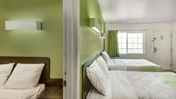 A hotel room with two beds, a window with curtains, and a door.