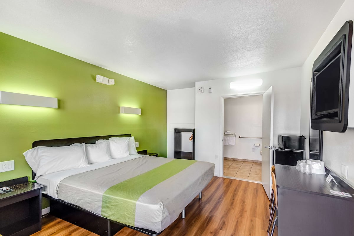 Habitación de hotel con cama, escritorio, televisión y baño visible a través de una puerta abierta.