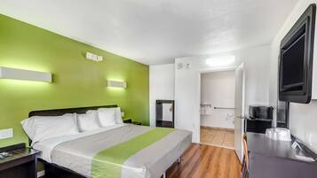 A hotel room with a bed, a desk, a TV, and a bathroom visible through an open door.
