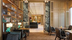 Un vestíbulo de hotel con mostrador de recepción, zona de estar y estantería con adornos.