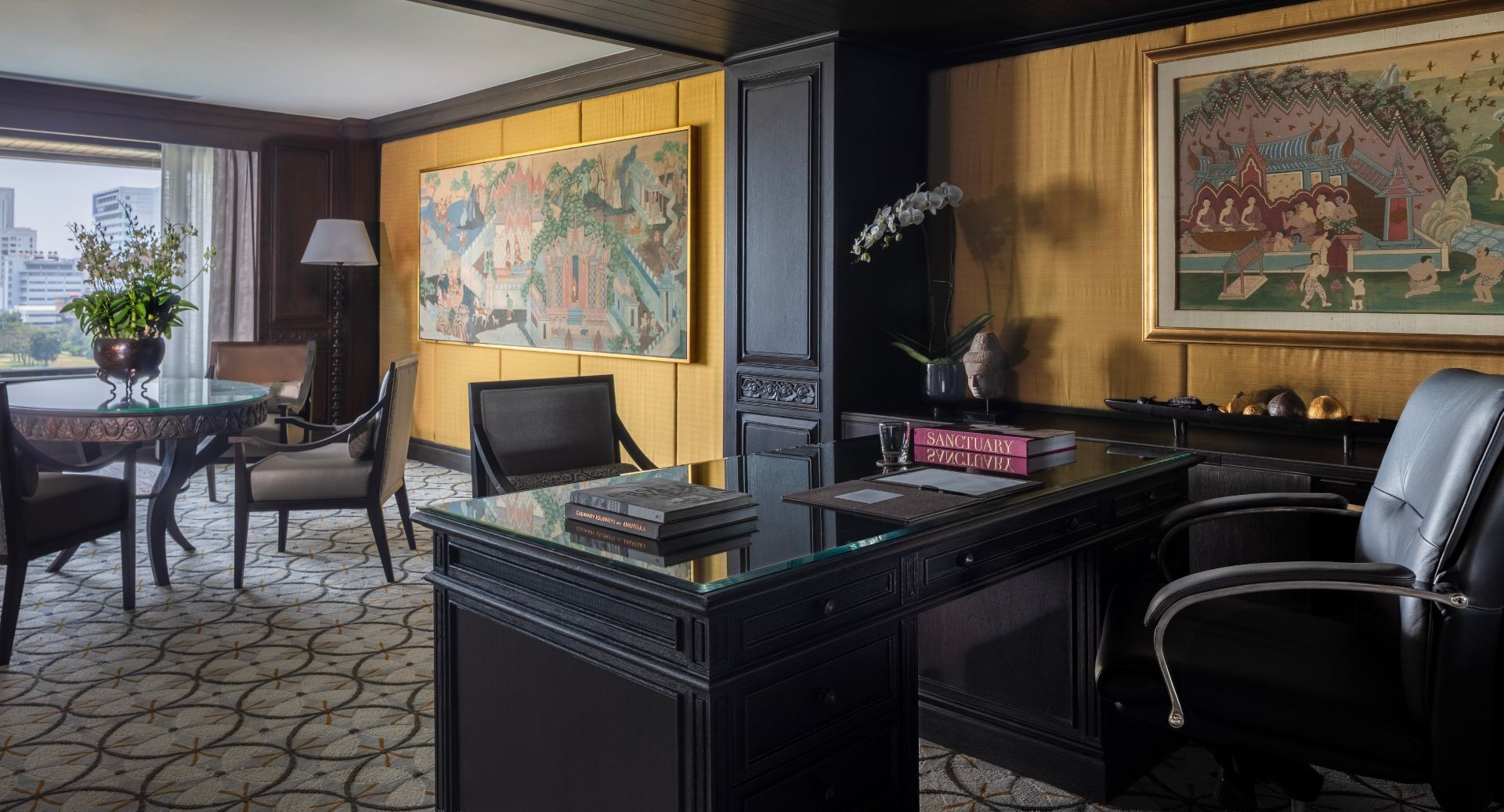 Een hotelkamer met een groot bureau, stoelen, een potplant, een schilderij en uitzicht op de stad.