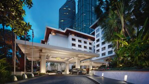 Un hotel moderno con un vestíbulo amplio, una entrada cubierta y vistas a edificios altos al fondo.