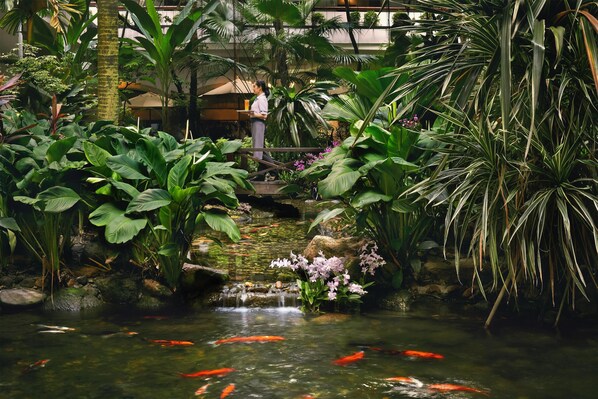 Un jardin intérieur paisible, avec un bassin à carpes koï, une végétation luxuriante et une petite cascade.
