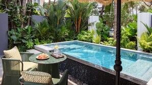 Una zona junto a la piscina con un espacio de descanso, una pequeña mesa con rodajas de sandía y un vaso de agua.