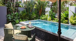 Ein Poolbereich mit Sitzgelegenheit, einem Tisch mit Wassermelone und einem Glas Wasser.